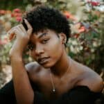 Close-up of a beautiful Black woman with natural curly hair, wearing a necklace, in a lush garden setting.