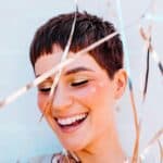 Playful celebration: woman with short hair, gold eyeshadow, and white details, surrounded by metallic ribbons, smiling brightly.